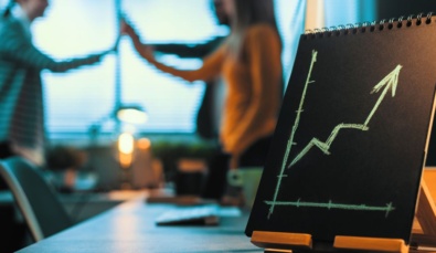 a graph on an ipad on a desk with an arrow pointing upwards and business people out of focus in the background used on a blog about ROCE Return on Capital Employed