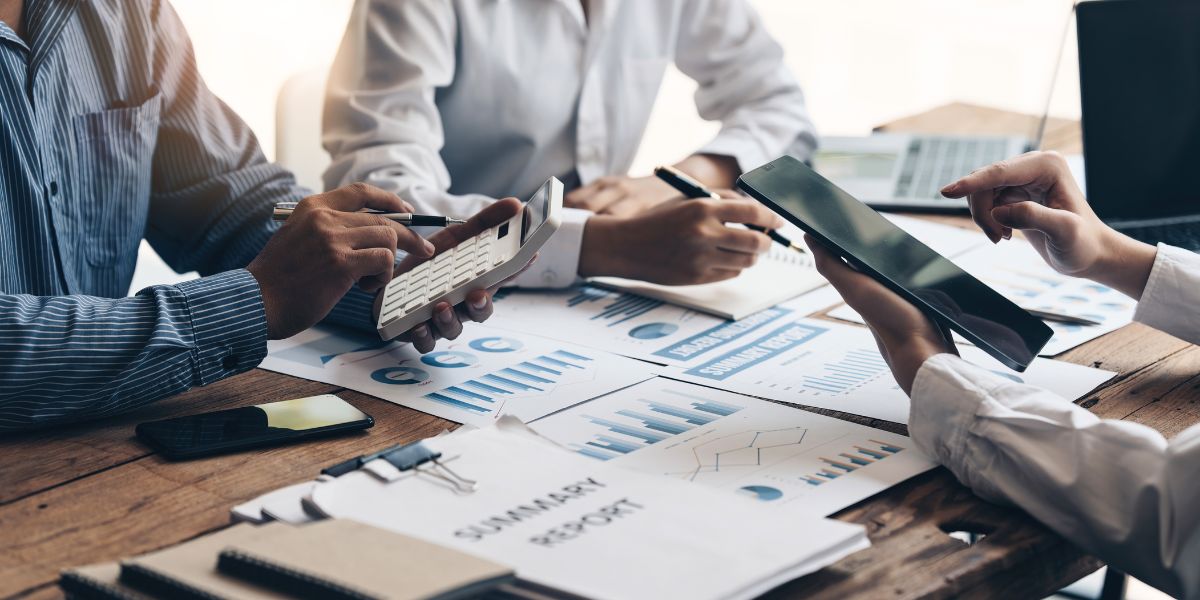 three faceless business people around a desk with charts and calculators used on a blog about how to get funding for a business