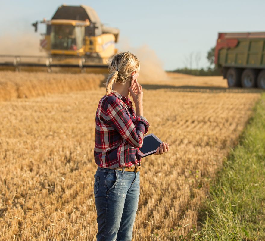 female farmer on phone to agribusiness accountant in a field with harvester | MGI