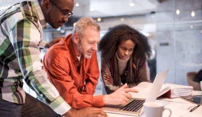 small team of 3 gathered round laptop | Minimise Impact Minimum Wage Increase