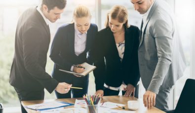 four business colleagues discussing government grant funding pointing at charts on table | MGI