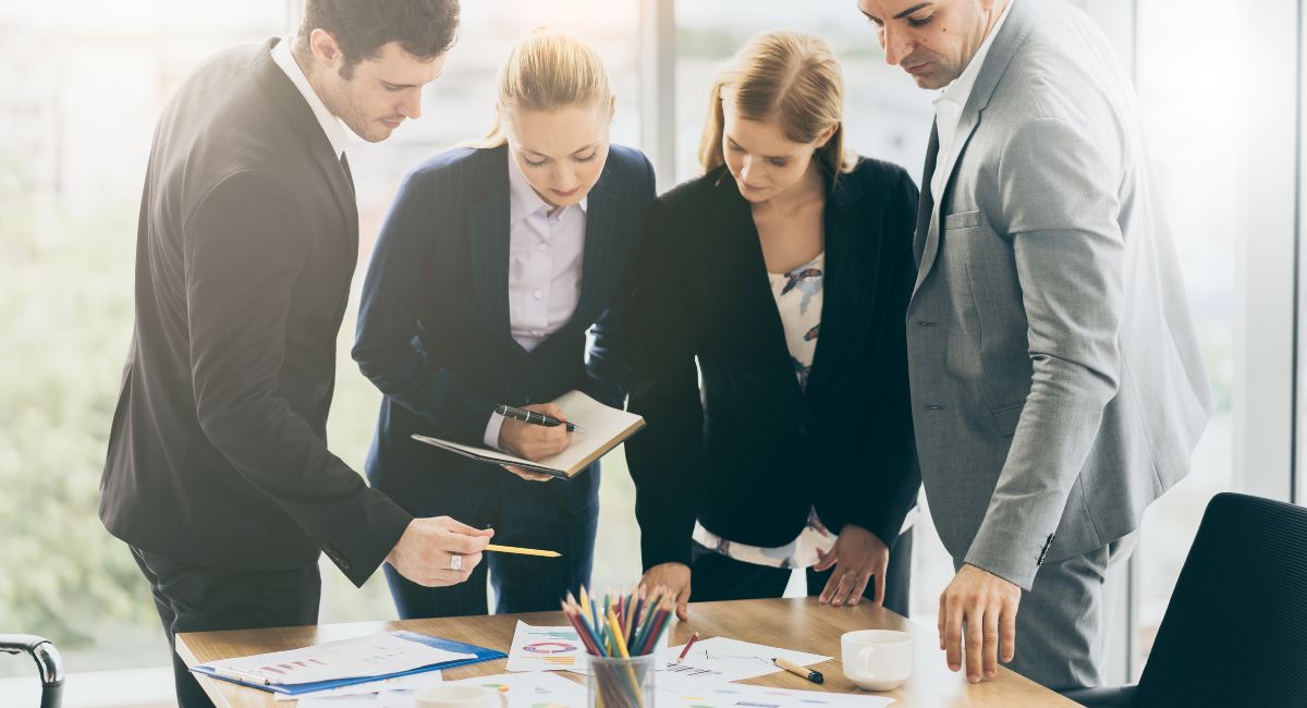 four business colleagues discussing government grant funding pointing at charts on table | MGI