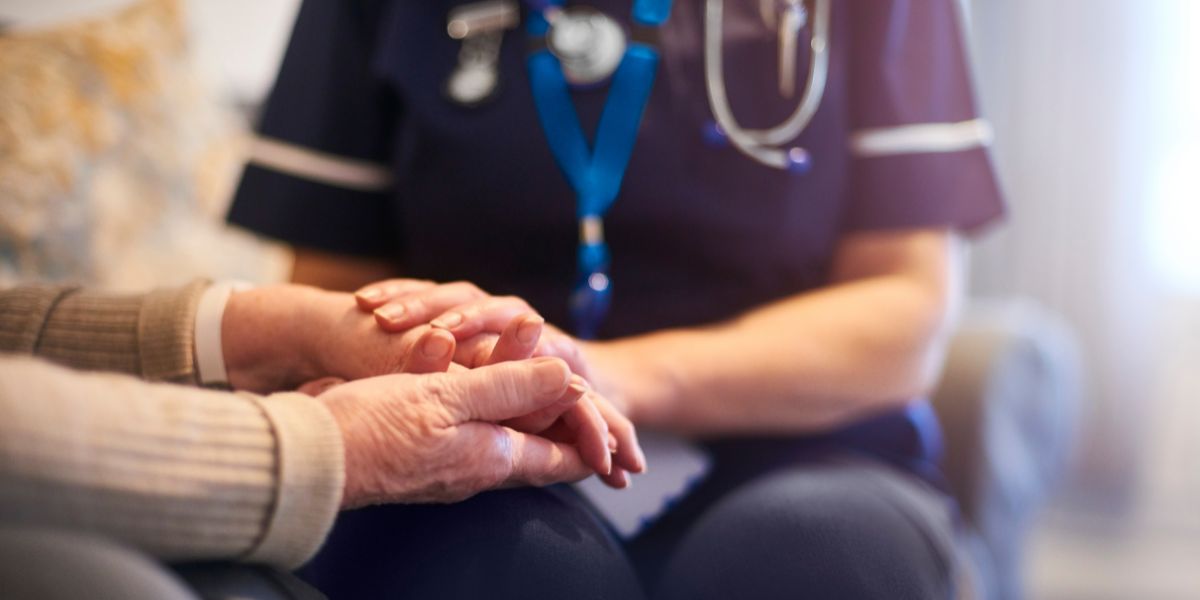 aged care nurses hands holding those of an elderly patient.