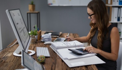 a woman sitting at a desk with a laptop, screen and financial documentsused on a blog about how to reduce tax