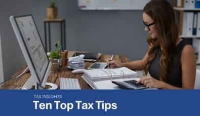 a woman sitting at a desk with a laptop, screen and financial documentsused on a blog about how to reduce tax