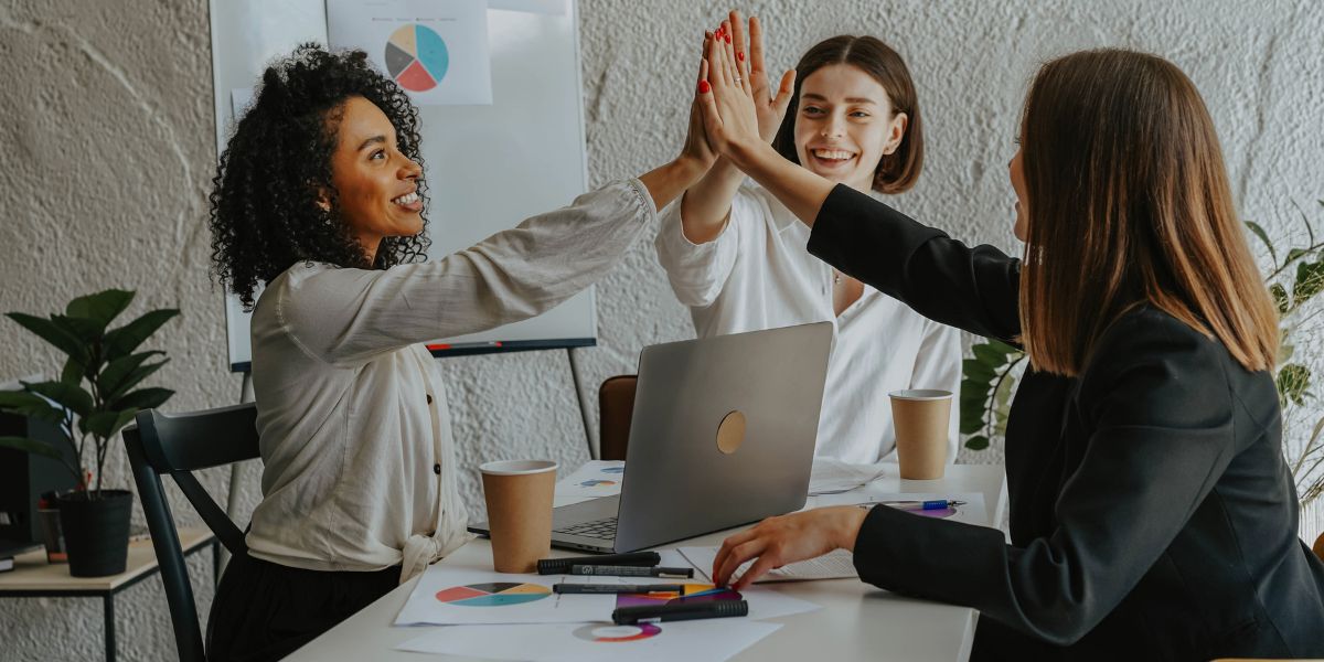 three business women doing a 'high five' around a table