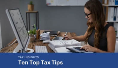 a woman sitting at a desk with a laptop, screen and financial documentsused on a blog about how to reduce tax